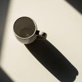 A ceramic cup with a handle sits on a light surface, casting a prominent shadow. The cup is Royalty Free Stock Photo