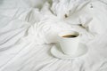 Ceramic cup of hot black coffee on messy bed sheet, in soft focus