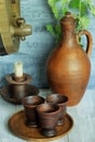 Wooden wine barrel, ceramic jug, plate with clay cups and ceramic candlestick with white candle on wooden rustic table against