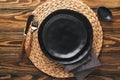 Ceramic empty black plate, silverware and linen kitchen towel napkin on old brawn wooden table background. Cooking stone backdrop Royalty Free Stock Photo