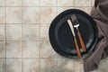 Ceramic empty black plate, silverware and linen kitchen towel napkin on old ceramic tile table background. Cooking stone backdrop Royalty Free Stock Photo