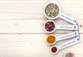 Ceramic measurement spoons filled with various spices on a pinewood background