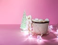 Ceramic mug with hot fresh cocoa drink and handmade funny marshmallow snowman on soft pink background