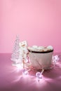 Ceramic mug with hot fresh cocoa drink and handmade funny marshmallow snowman on soft pink background