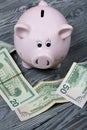 Ceramic piggy bank in the form of a pink pig. Nearby are dollar bills. Against the background of aged wooden boards with a black Royalty Free Stock Photo