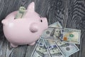 Ceramic piggy bank in the form of a pink pig. Nearby are dollar bills. One of them sticks out of the piggy bank. Against the Royalty Free Stock Photo