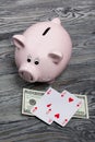 Ceramic piggy bank in the form of a pink pig. Nearby are dollar bills and playing cards. Against the background of aged wooden Royalty Free Stock Photo