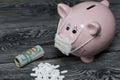 Ceramic piggy bank in pink. With a gauze bandage. In front of her is a handful of white pills. Lay dollar bills, rolled up into a Royalty Free Stock Photo
