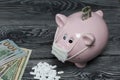 Ceramic piggy bank in pink. With a gauze bandage. Near it lie dollar bills, one of them sticks out of the slot. In front of her is Royalty Free Stock Photo