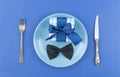 Ceramic plate with a cutlery and gift box on the blue paper background Royalty Free Stock Photo