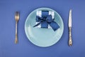 Ceramic plate with a cutlery and gift box on the blue paper background Royalty Free Stock Photo