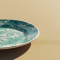 A ceramic plate with a green and white floral pattern rests on a sandy surface. The Royalty Free Stock Photo