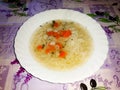 Ceramic plate of noodle soup with carrot and garlic, all on a tablecloth with a predominant purple motif Royalty Free Stock Photo