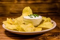 Ceramic plate with potato chips and glass bowl with sour cream on wooden table Royalty Free Stock Photo