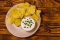 Ceramic plate with potato chips and glass bowl with sour cream on wooden table. Top view Royalty Free Stock Photo