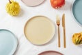 Ceramic plates with fork and knife and pumpkins serving background on white tablecloth. Top view, mockup