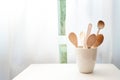 Ceramic pot with wooden cooking spoons on a table in front of the kitchen window with white curtains, copy space Royalty Free Stock Photo