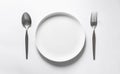 Ceramic round dish with silver fork and spoon, on white table Royalty Free Stock Photo