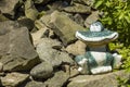 Ceramic smiling frog sitting on a pile of stones and next to green plants in a garden