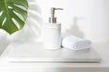 Ceramic soap dispenser and folded towel on white marble stand