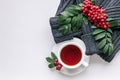 Ceramic teacup on white served table. Herbal tea in porcelain mug with saucer. Knitted sweater, rowan branch and rowanberry flat Royalty Free Stock Photo