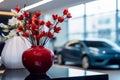 Ceramic vase holds fake red flowers on a glass table, showroom elegance.