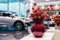 Ceramic vase holds fake red flowers on a glass table, showroom elegance.