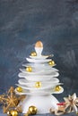 Ceramic white dishes Christmas tree with yellow gold Xmas balls and decoration on dark background. Vertical. Creative Royalty Free Stock Photo