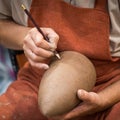 Ceramic workshop, the master puts otnament on unfired earthenware jug. Close-up of master hands. Made by hand, a hobby. Background