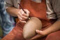 Ceramic workshop, the master puts otnament on unfired earthenware jug. Close-up of master hands. Made by hand, a hobby. Background