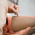 Ceramic workshop, the master puts otnament on unfired earthenware jug. Close-up of master hands. Made by hand, a hobby. Background