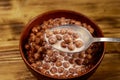 Cereal chocolate balls with milk in a bowl on wooden table. Spoon with breakfast