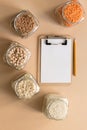 Cereals in glass jars on the table next to a Notepad and pencil. Space for text, white sheet of paper.