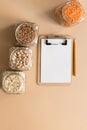 Cereals in glass jars on the table next to a Notepad and pencil. Space for text, white sheet of paper.