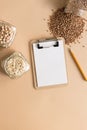 Cereals in glass jars on the table next to a Notepad and pencil. Space for text, white sheet of paper.