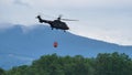 Fire helicopter flying over a forest with bucket full of water to drop on fire