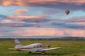 Cessna airplane in field at sunrise with hot air balloon in sky