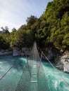 Cesspool Gorge hanging swing bridge leading over turquoise crystal clear blue Arahura River, West Coast, New Zealand