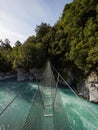 Cesspool Gorge hanging swing bridge leading over turquoise crystal clear blue Arahura River, West Coast, New Zealand