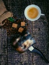 Cezve, a cup of coffee, a bag of spilled coffee beans and cane sugar lumps on an old wooden surface Royalty Free Stock Photo