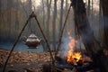 chai tea kettle hanging from a tripod over a crackling campfire