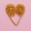 A gold chain laid out in the shape of a heart on a pink background Royalty Free Stock Photo