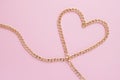 A gold chain laid out in the shape of a heart on a pink background Royalty Free Stock Photo