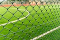 Through the chain-link fence, a blurred soccer field emerges, where passion for the game and dreams of victory come to