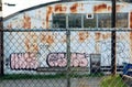 Chain link fence enclosure around graffiti marked building.