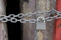 A chain of silver color with closed padlock on an old gate. Closeup of old wooden door with closed padlock on a chain. Royalty Free Stock Photo