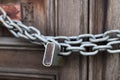 A chain of silver color with closed padlock on an old gate. Closeup of old wooden door with closed padlock on a chain. Royalty Free Stock Photo