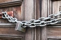 A chain of silver color with closed padlock on an old gate. Closeup of old wooden door with closed padlock on a chain.