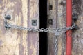 A chain of silver color with closed padlock on an old gate. Closeup of old wooden door with closed padlock on a chain. Royalty Free Stock Photo