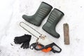 chainsaw, pare of gloves, two boots and log on the snowy background